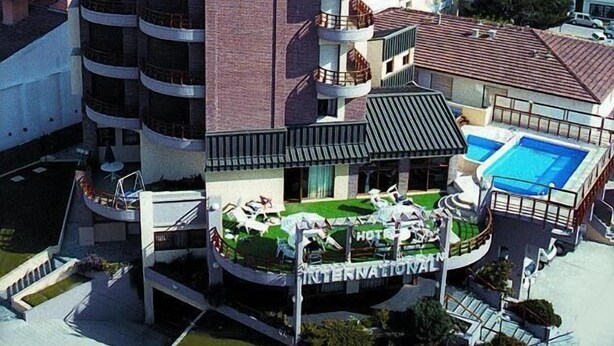 A multi-story hotel with a prominent clock tower, a rooftop pool, and a landscaped garden area. - Hotel Gran International (Villa Gesell)