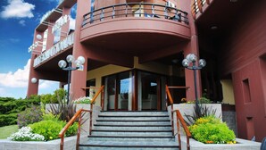 A multi-story building with a curved balcony, a staircase leading to the entrance, and a well-maintained garden area. - Hotel Gran International (Villa Gesell)