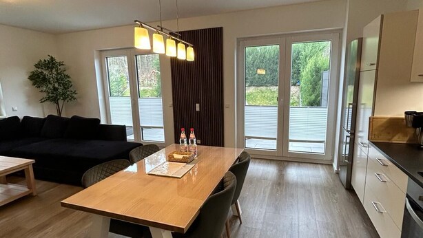 Une cuisine moderne avec une table en bois, des chaises noires et un luminaire suspendu.