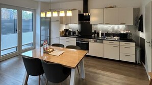Une cuisine moderne avec des meubles blancs, une table à manger en bois et des luminaires suspendus.