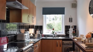 Une cuisine moderne avec des meubles en bois, un four encastré, un lave-vaisselle et une fenêtre donnant sur un paysage verdoyant.
