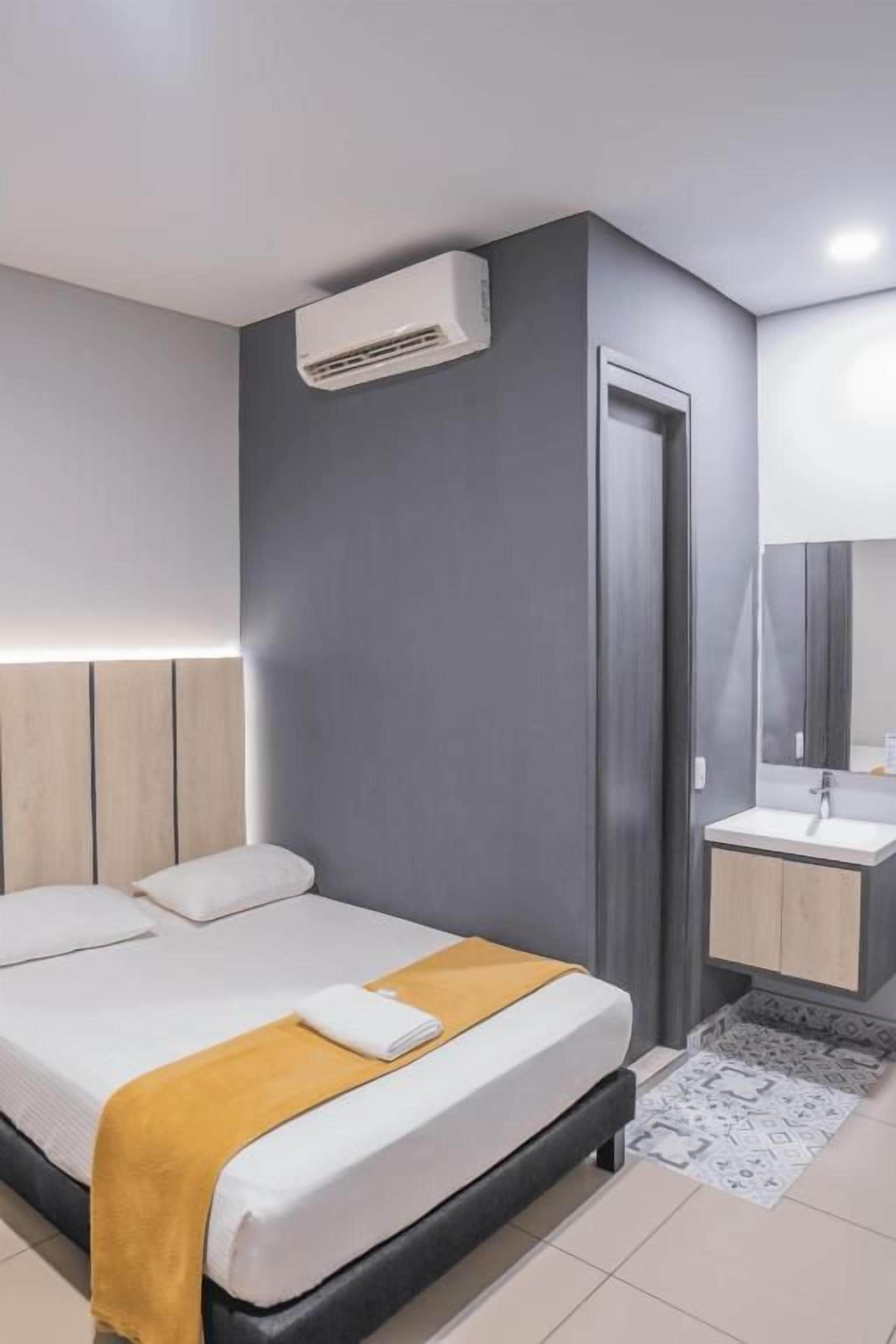 A modern hotel room with a bed, bedside table, and a built-in air conditioning unit.