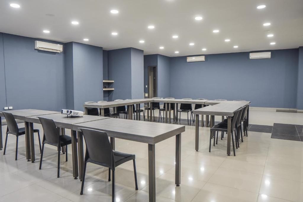 A conference room with multiple tables and chairs, air conditioning units, and a tiled floor.