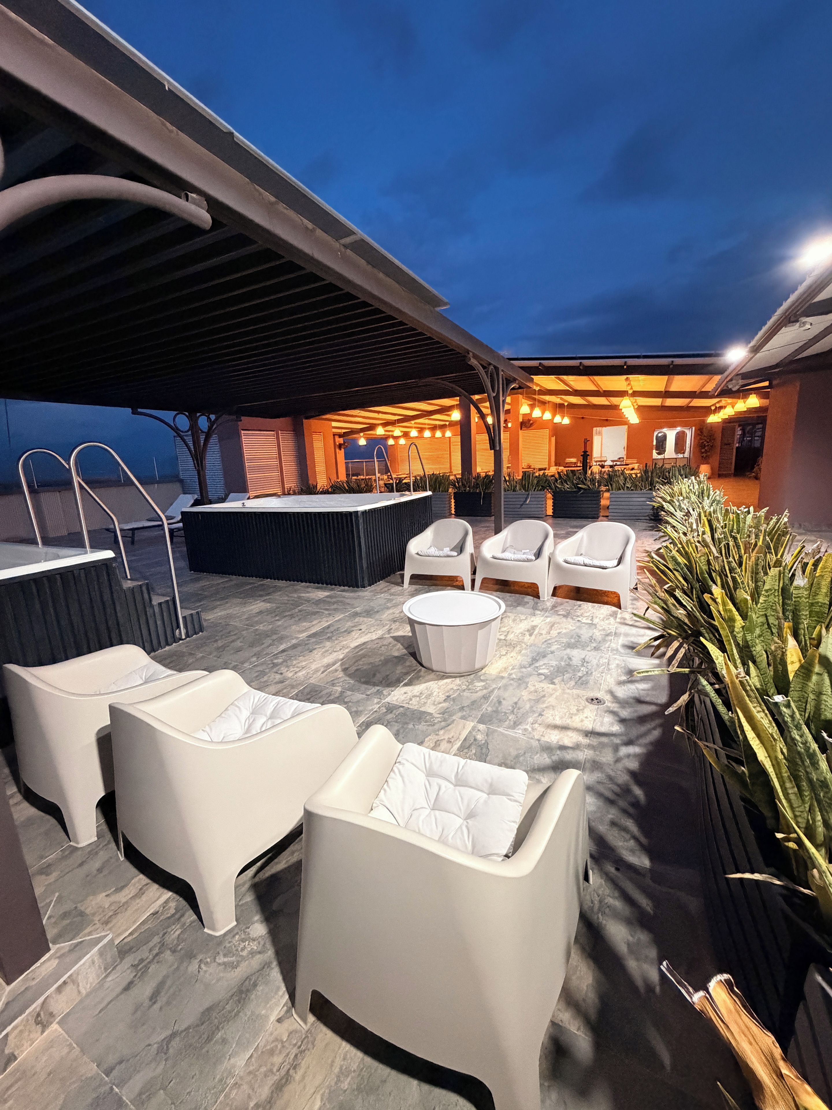 An outdoor patio area with seating, a hot tub, and ambient lighting.