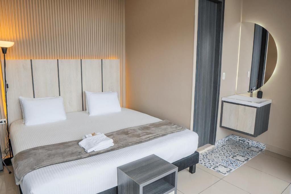 Une chambre d’hôtel avec un grand lit, une table de chevet, un miroir et une petite armoire.