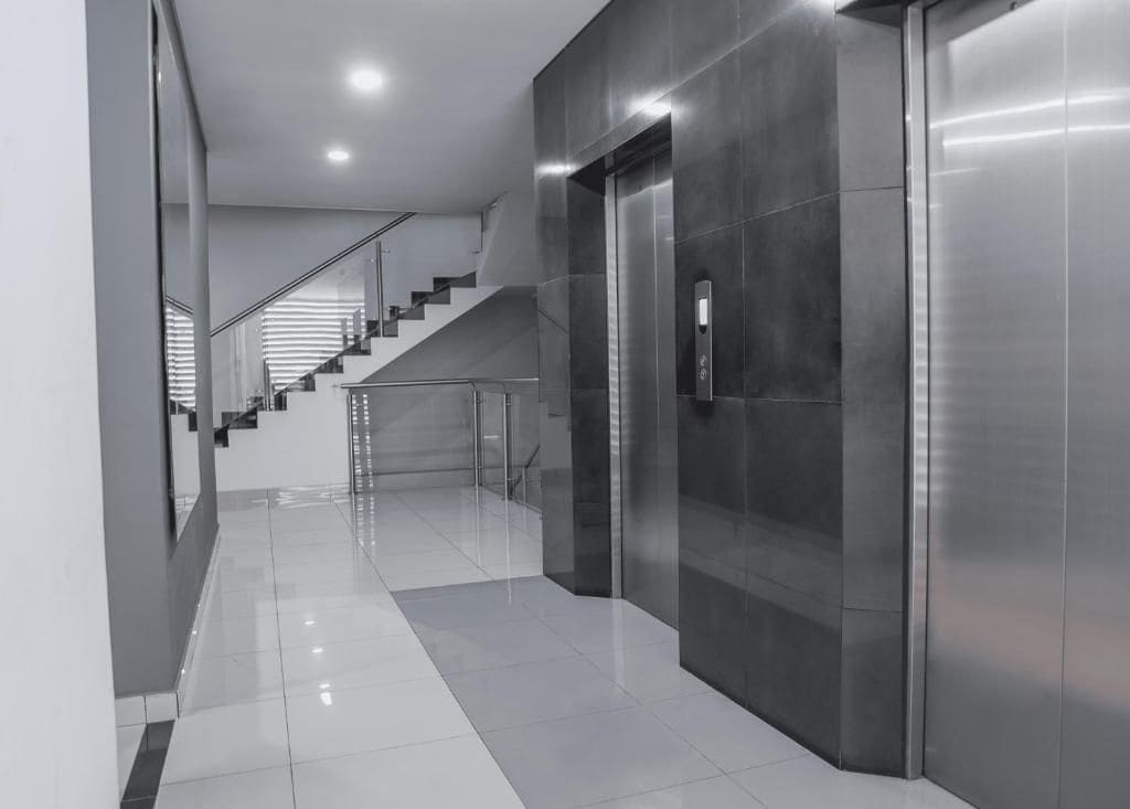 A modern interior with a staircase, elevator, and reflective floor.