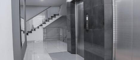 A modern interior with a staircase, elevator, and reflective floor.