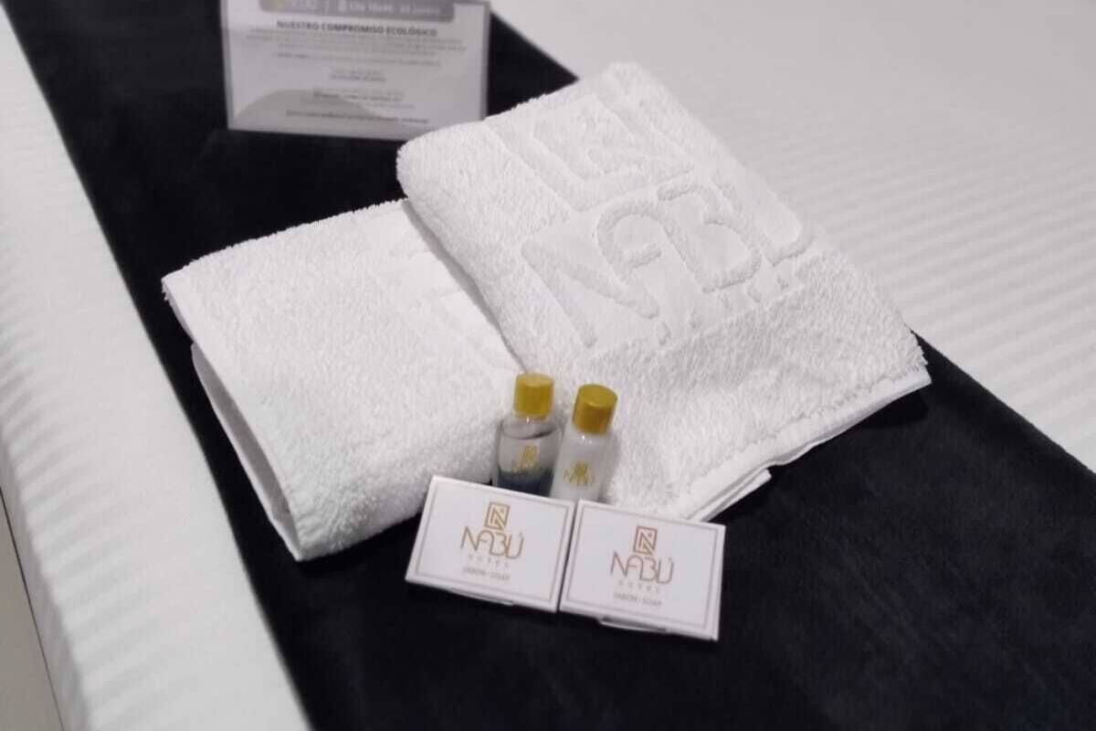 A neatly made bed with a white towel, two small bottles, and a card on a black bedspread.