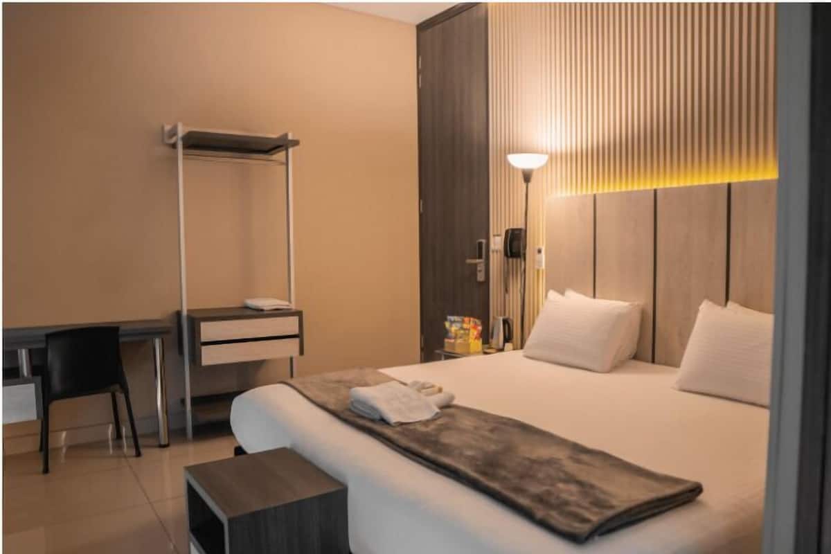 A hotel room with a bed, bedside table, desk, chair, and a lamp.