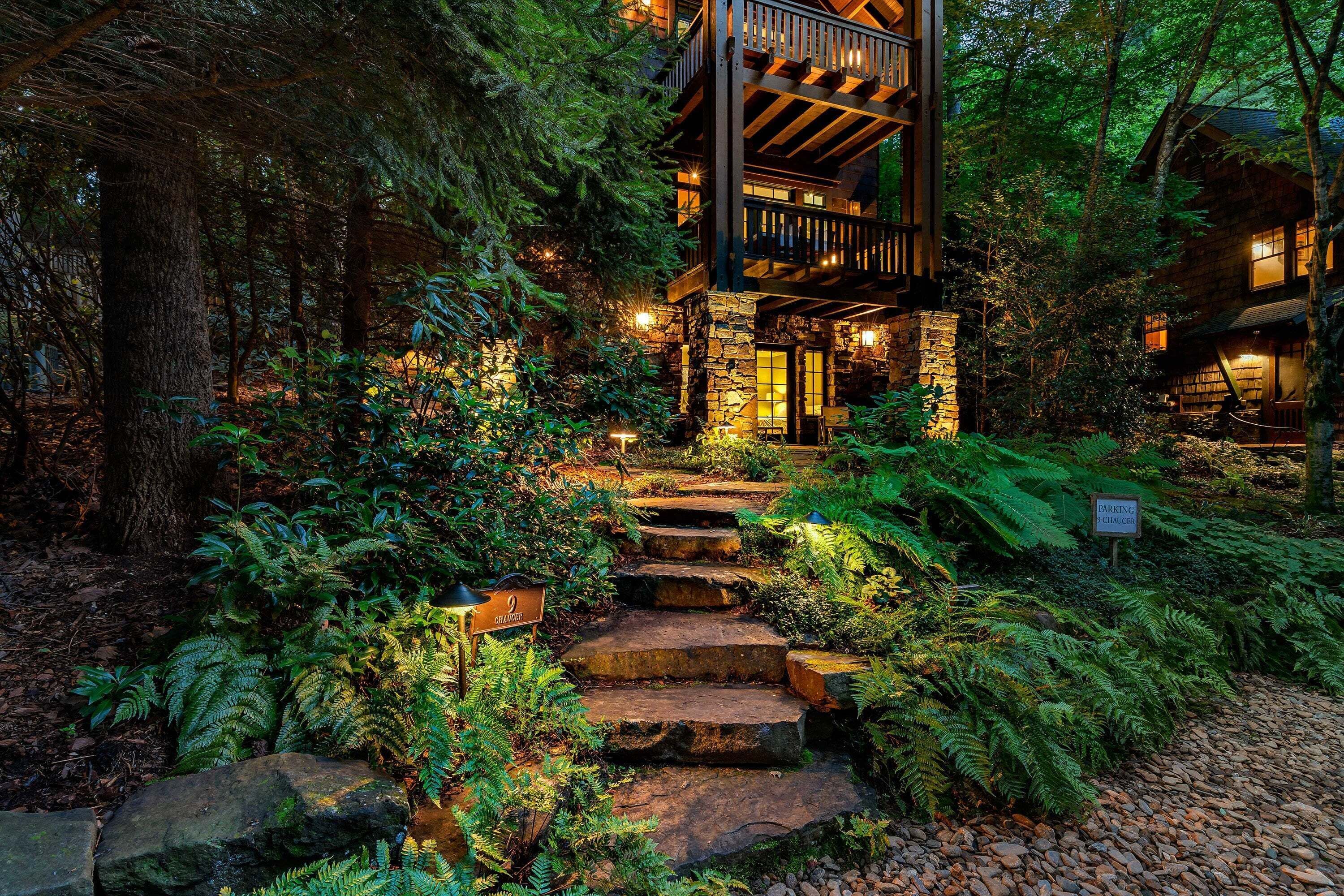 A wooden cabin with a stone staircase leading to a deck, surrounded by dense forest.