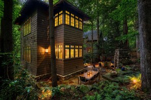 A cabin with a stone foundation, surrounded by a forest.