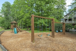 A playground with a swing set and a slide, surrounded by trees and a house in the background. - Wooded Treehaus in Cheshire Village | Dual King Suites, Viking Kitchen & Outdoor Fireplace (Black Mountain)