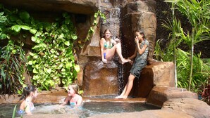 A natural water feature with a waterfall and rock formations, surrounded by lush greenery.