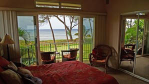 A bedroom with a large bed, a guitar, and a view of the ocean through a sliding glass door.