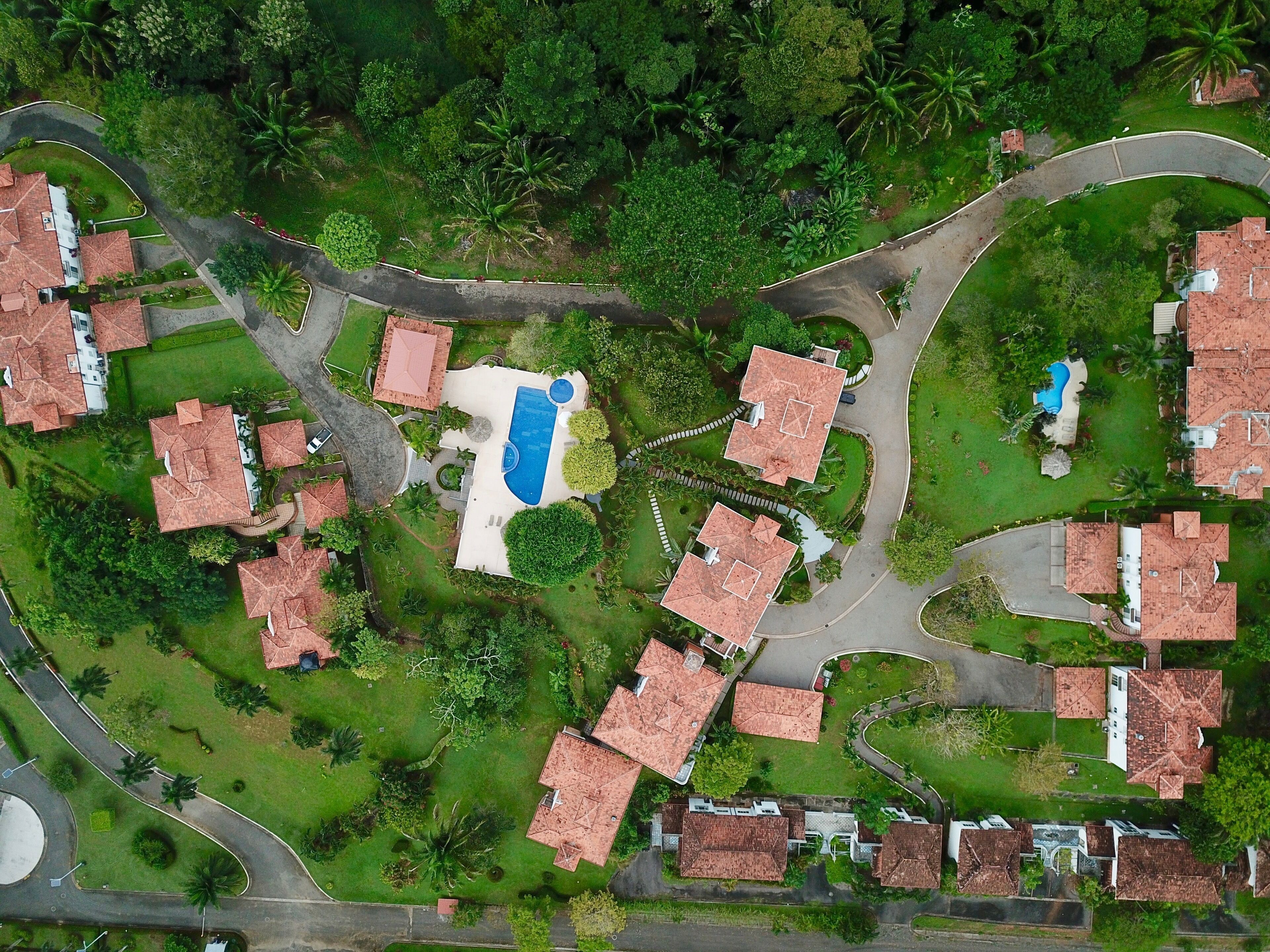 Vue aérienne d’un quartier résidentiel avec de nombreuses maisons, une piscine centrale et de la végétation luxuriante tout autour.