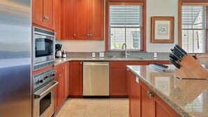Una cocina moderna con electrodomésticos de acero inoxidable, armarios de madera, encimera de granito y un block de cuchillos empotrado.