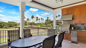 Un espacio de comedor al aire libre cubierto, con vista a un campo de golf y palmeras.