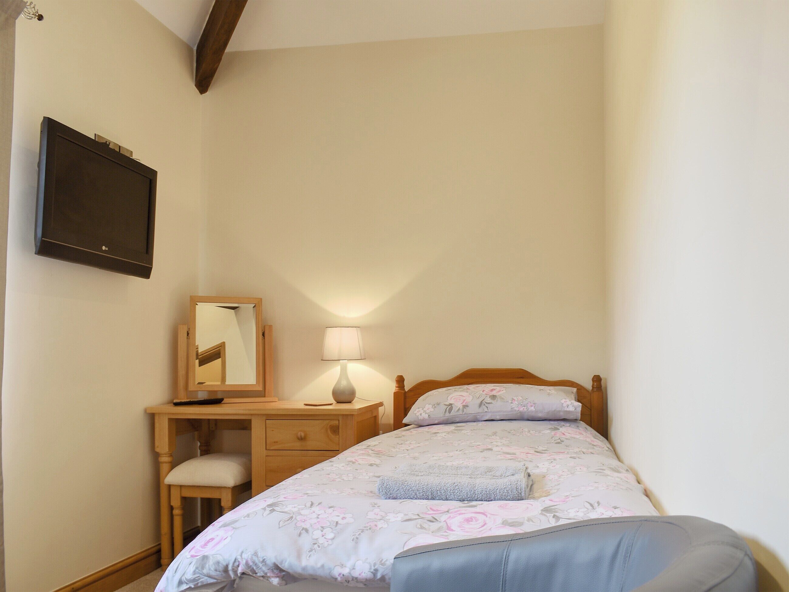 A bedroom with a bed, a desk, a chair, a lamp, and a mirror.