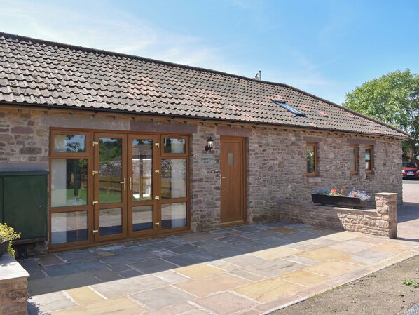 A stone building with a tiled roof, a wooden door, and large windows.