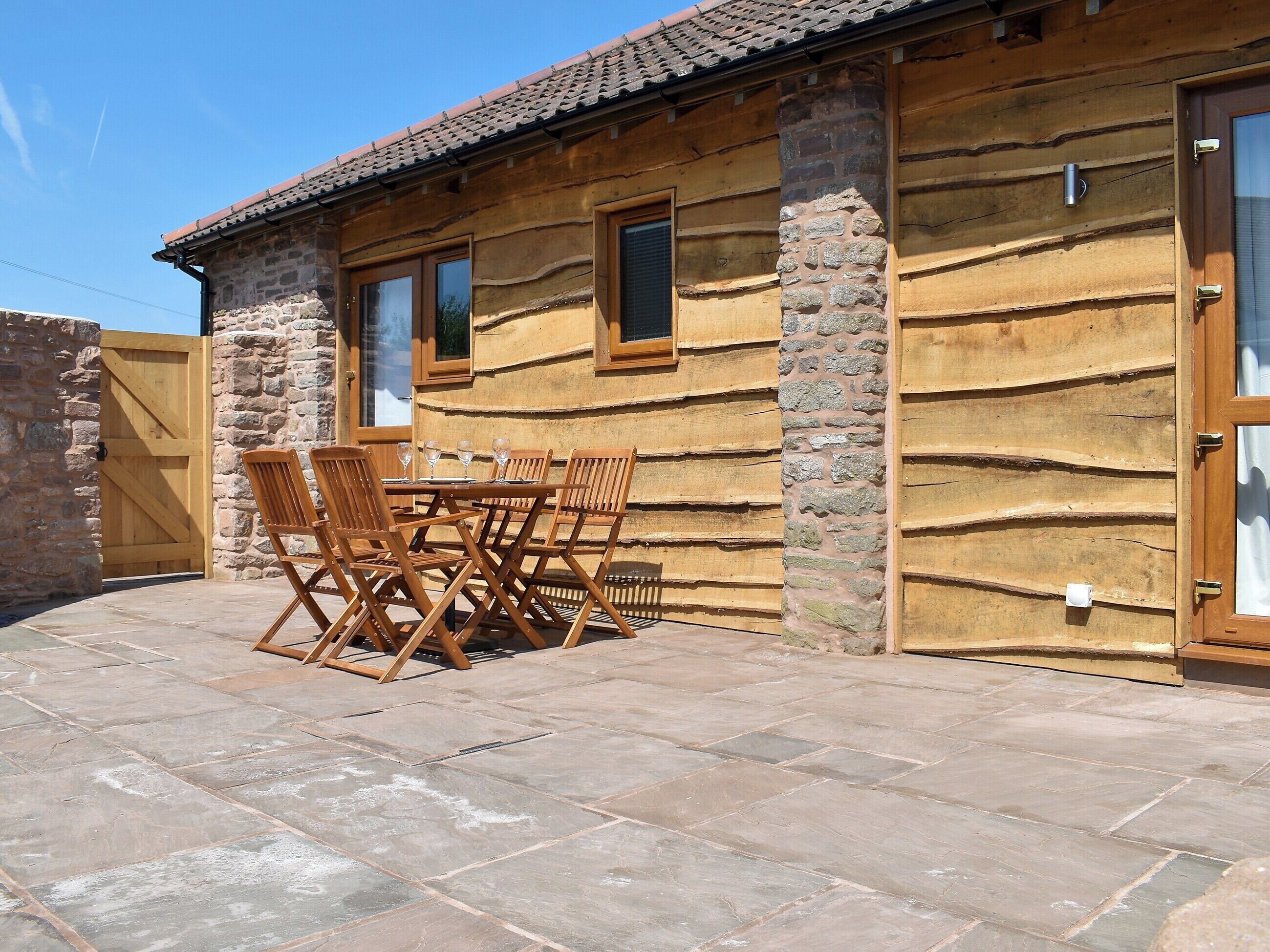 Een rustieke houten chalet met een stenen gevel, een houten deur en een terras met een tafel en stoelen.