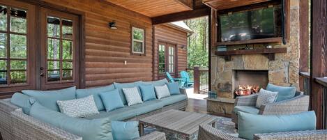 A log cabin with a stone fireplace, a large sofa, and wicker furniture.