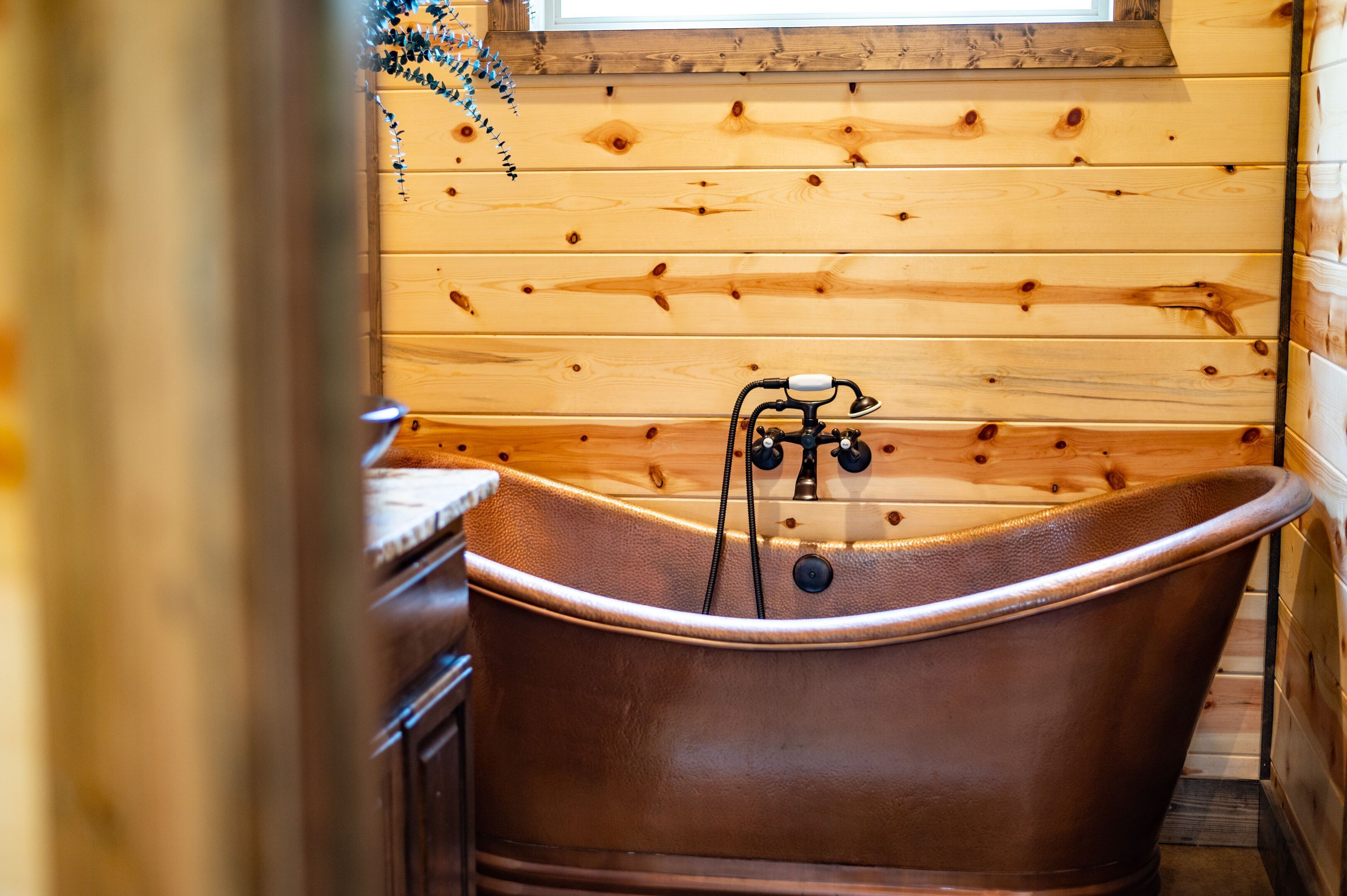 L’intérieur d’un chalet en bois, avec une baignoire sur pieds, des murs en bois et une fenêtre.