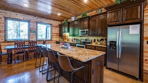 A wooden cabin interior with a kitchen featuring dark cabinets, stainless steel appliances, a granite countertop, and a bar area with stools.