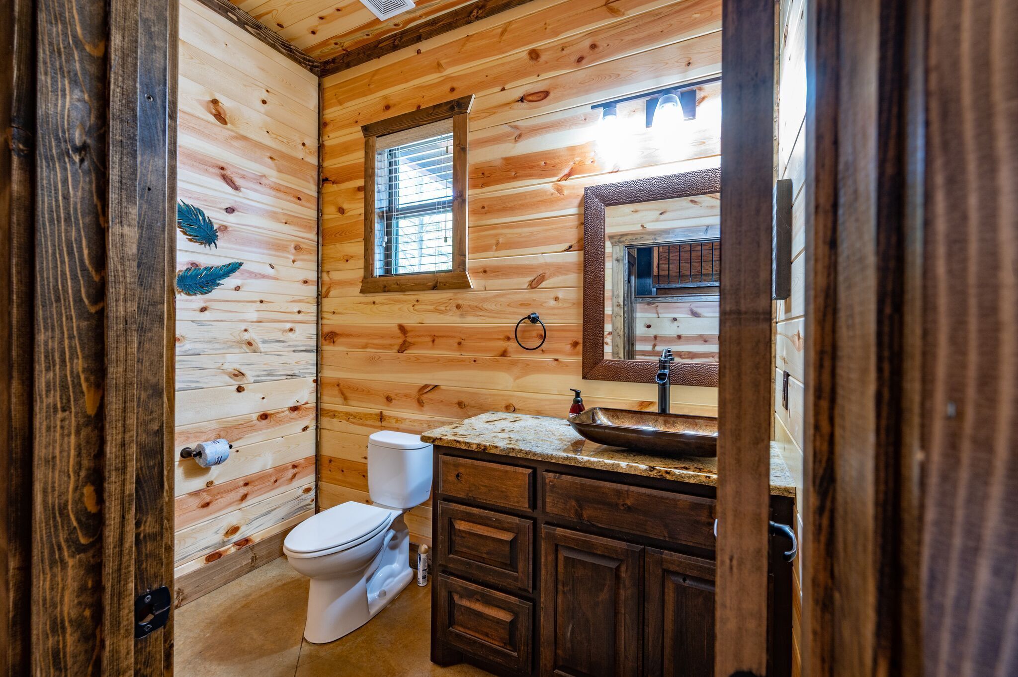 Baño de cabaña de madera con inodoro, lavamanos y ventana.