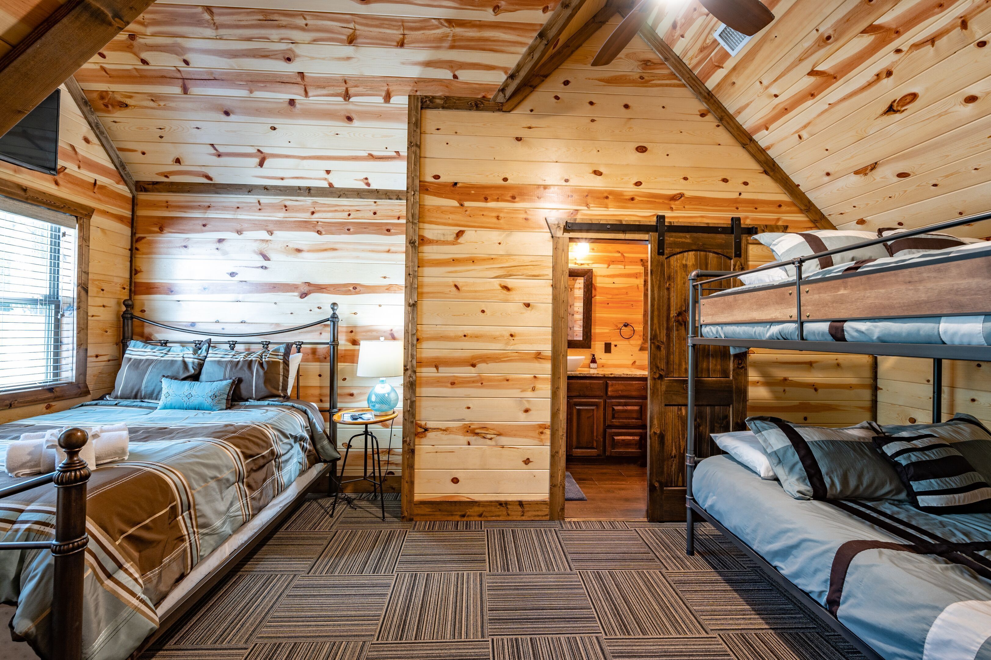Eine Holzhütte mit einem Etagenbett, einem Einzelbett und einem kleinen Tisch mit einer Lampe.