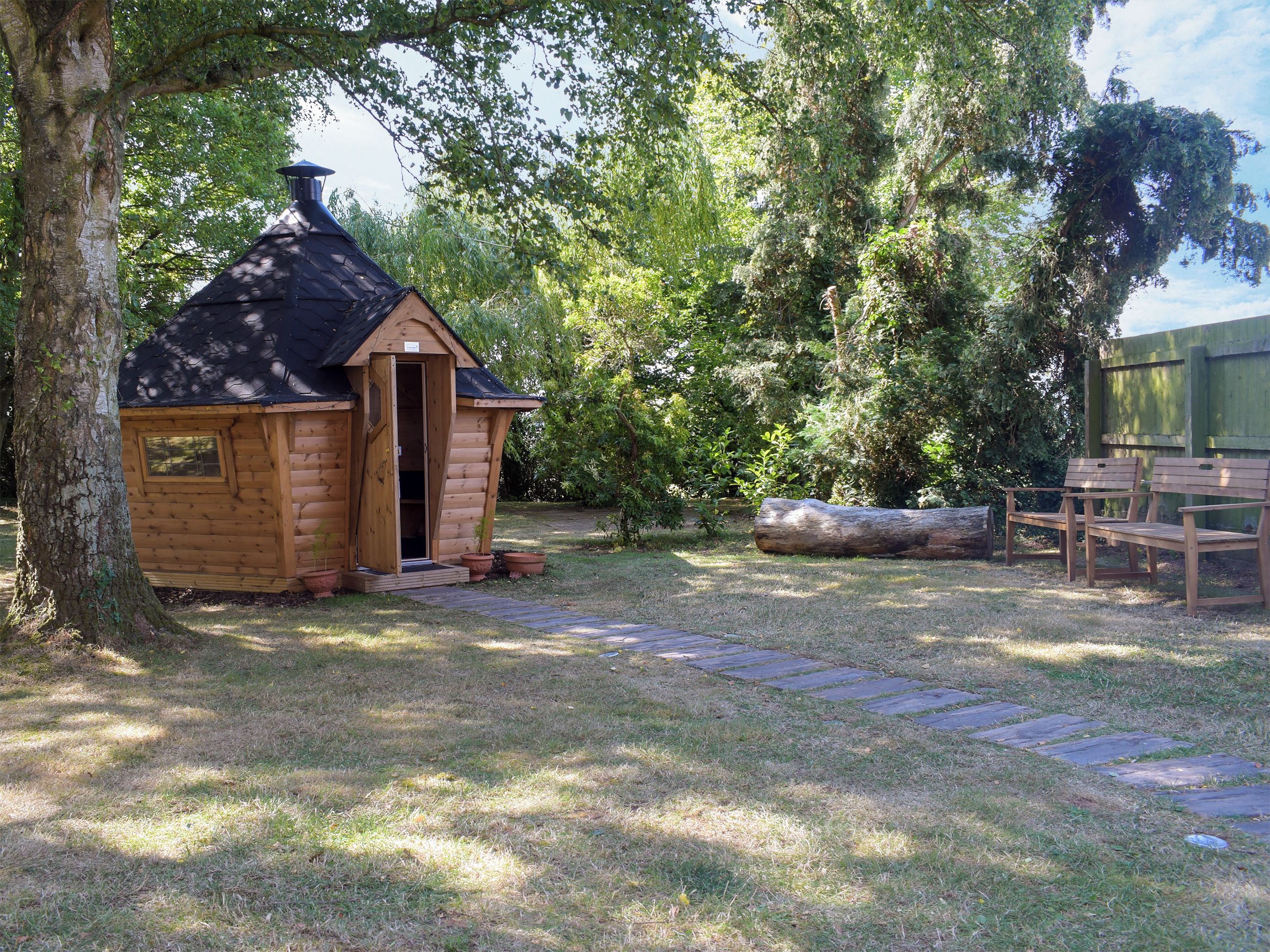 A wooden cabin with a door open, surrounded by trees and a stone pathway.