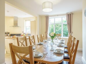 A dining area with a round table set for six, wooden chairs, and a view of the kitchen and greenery outside. - 5 bedroom accommodation in Crossway Green, near Stourport-on-Severn (Crossway Green, near Stourport-on-Severn)