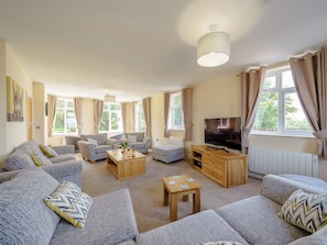A living room with sofas, a coffee table, a TV, and large windows with curtains.