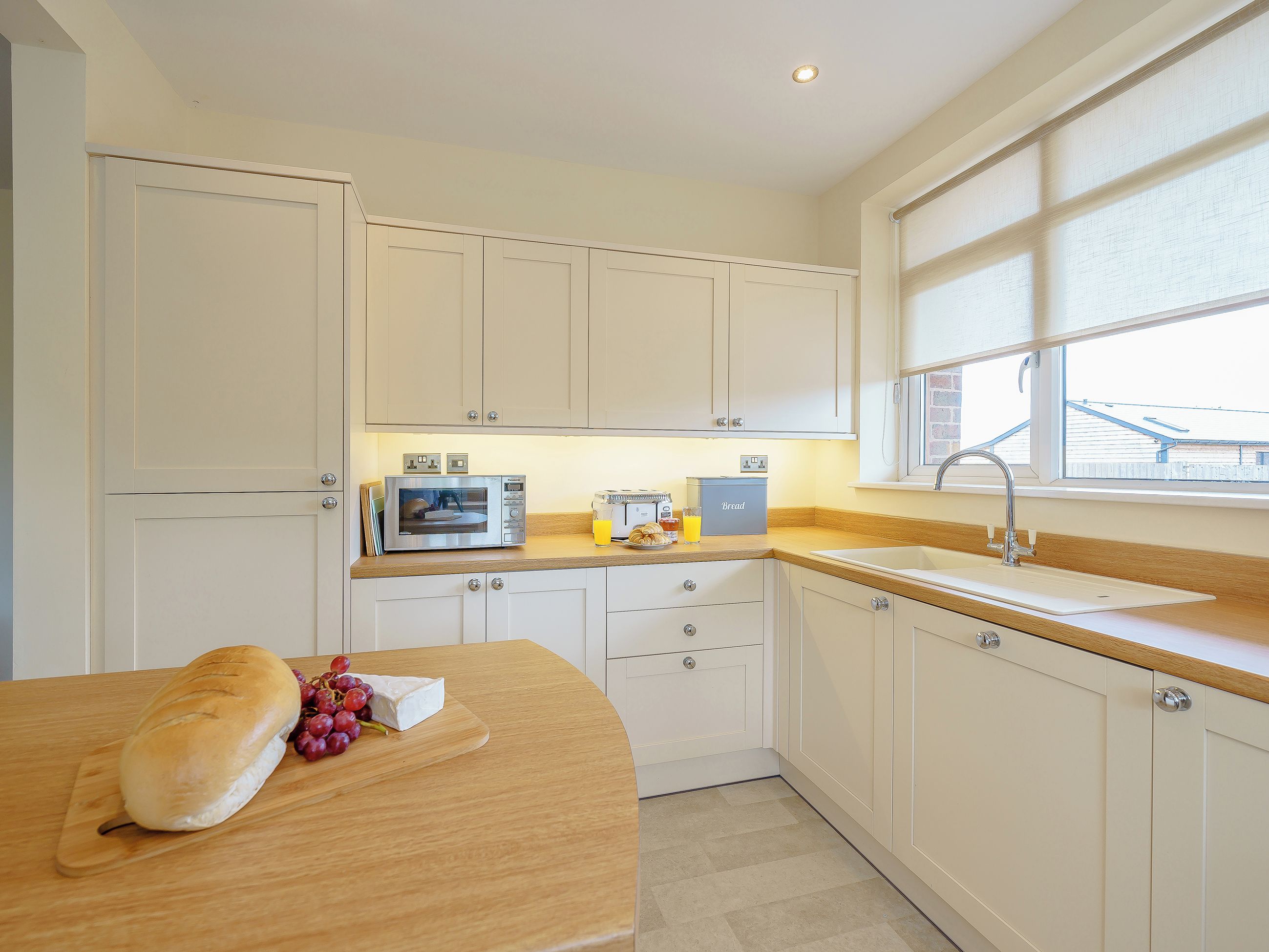 A kitchen with white cabinets, a microwave, a bread box, and a window with a view.