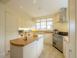 A modern kitchen with white cabinets, a central island, a stove, and a window providing natural light. - 5 bedroom accommodation in Crossway Green, near Stourport-on-Severn (Crossway Green, near Stourport-on-Severn)