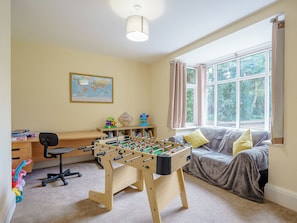 A room with a foosball table, a desk with a computer, a chair, a sofa, a window with curtains, and a map on the wall.
