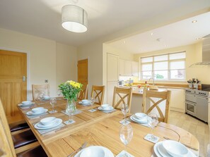 A dining area with a wooden table set for six, a vase with flowers, and a kitchen in the background. - 5 bedroom accommodation in Crossway Green, near Stourport-on-Severn (Crossway Green, near Stourport-on-Severn)