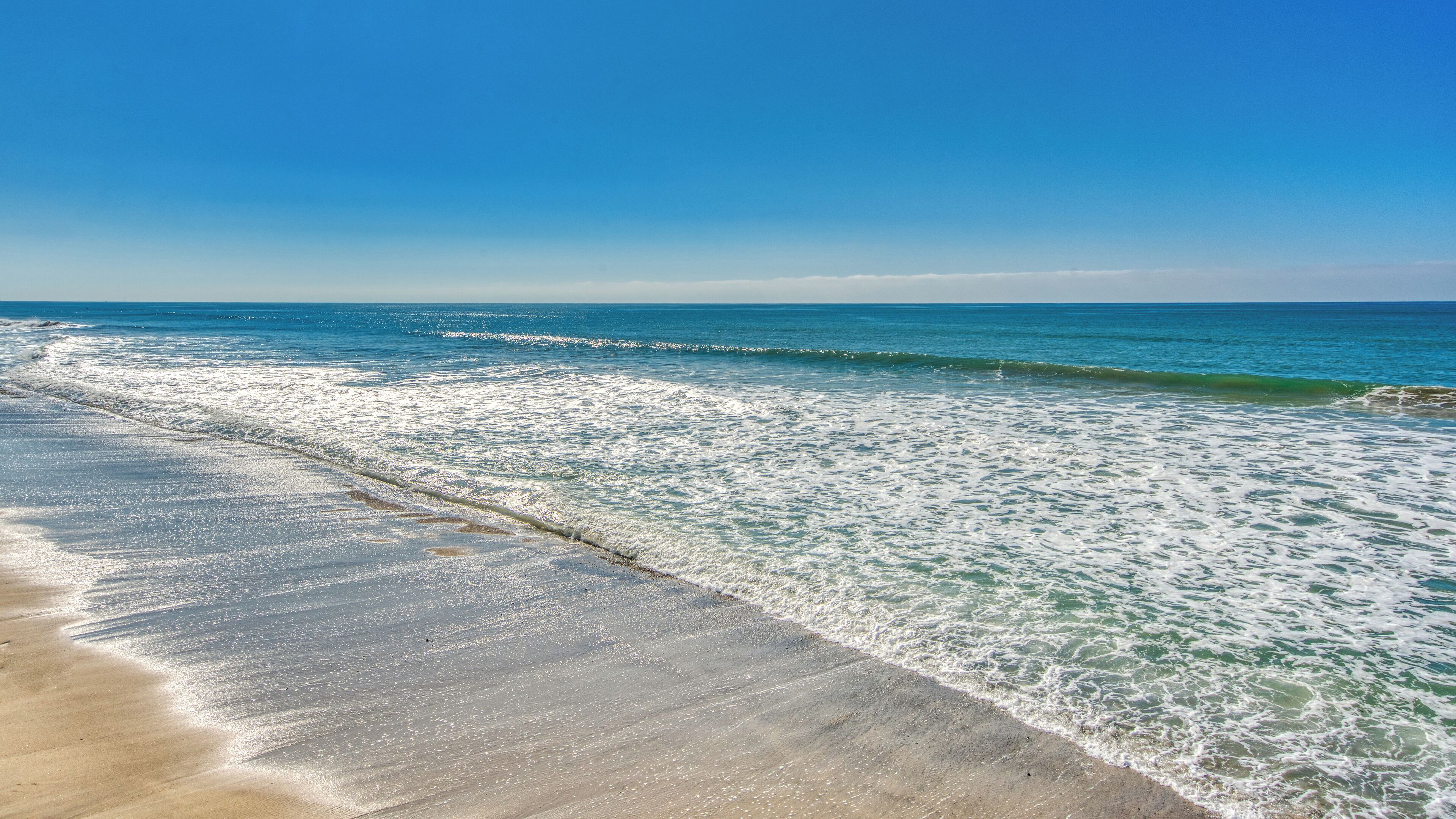Ein Strand mit klarem, blauem Wasser und einem sandigen Ufer.