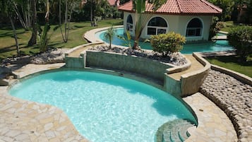 Relax by the serene pool surrounded by lush gardens and a charming Mediterranean-style building.