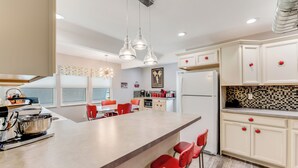 A modern kitchen with a large island, red bar stools, and a dining area with orange chairs. -  Sleeps 12•Huge PrivateDeck•Beach Gear•Pool Table•Steps to Ocean•Trailer parking (Ormond Beach)