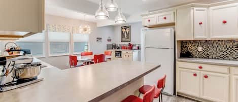 A modern kitchen with a large island, red bar stools, and a dining area with orange chairs.