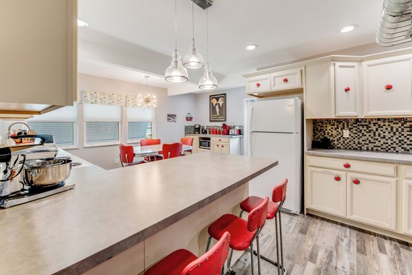 A modern kitchen with a large island, red bar stools, and a dining area with orange chairs. - Sleeps 12•Huge PrivateDeck•Beach Gear•Pool Table•Steps to Ocean•Trailer parking (Ormond Beach)