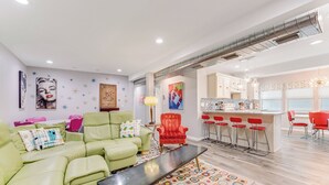 A modern living room with a green sofa, a red chair, and a bar area with red bar stools. -  Sleeps 12•Huge PrivateDeck•Beach Gear•Pool Table•Steps to Ocean•Trailer parking (Ormond Beach)