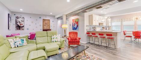 A modern living room with a green sofa, a red chair, and a bar area with red bar stools.