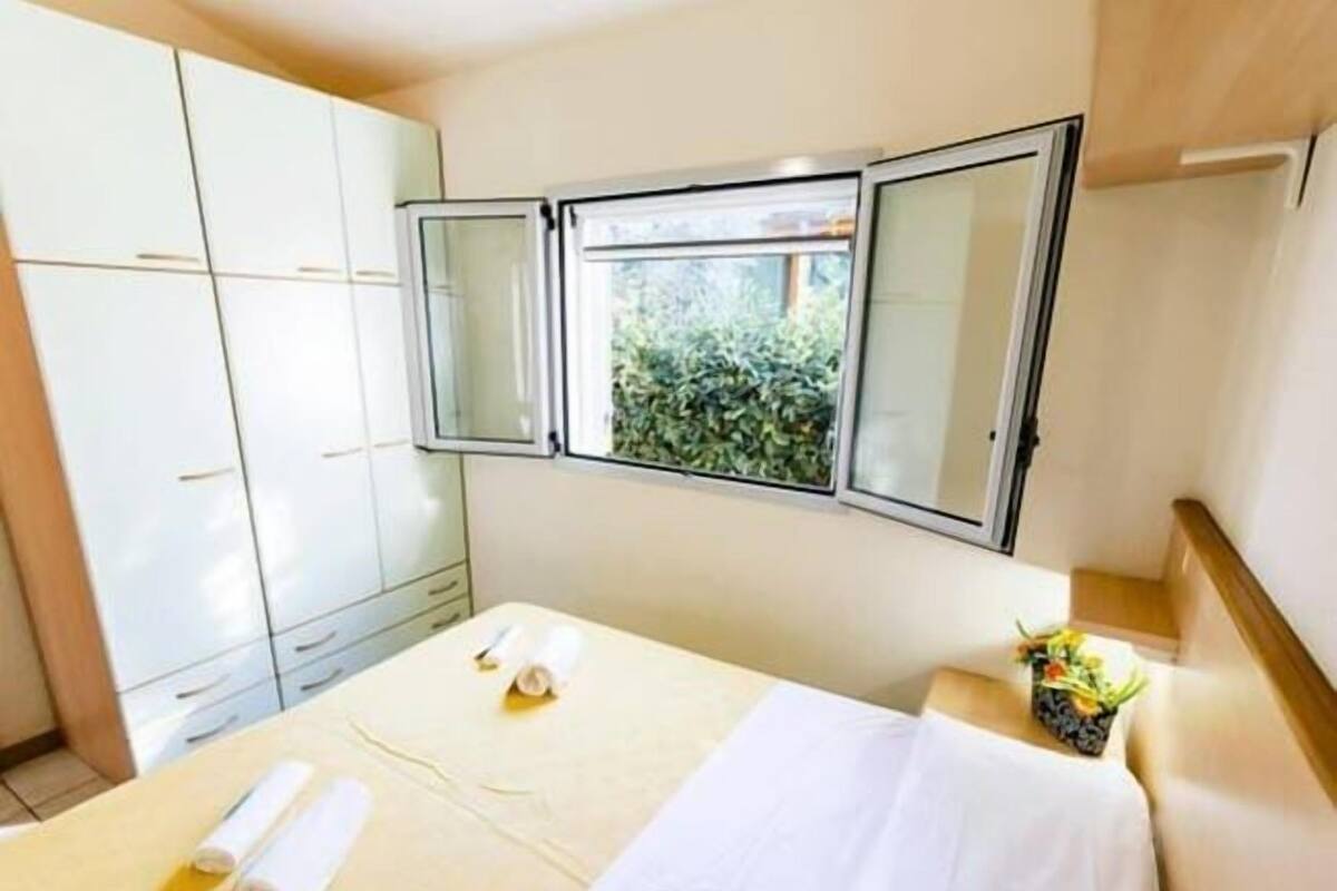 Ein Hotelzimmer mit Bett, Fenster mit Blick auf Grünflächen, einem Kleiderschrank und einem kleinen Tisch mit Pflanze.