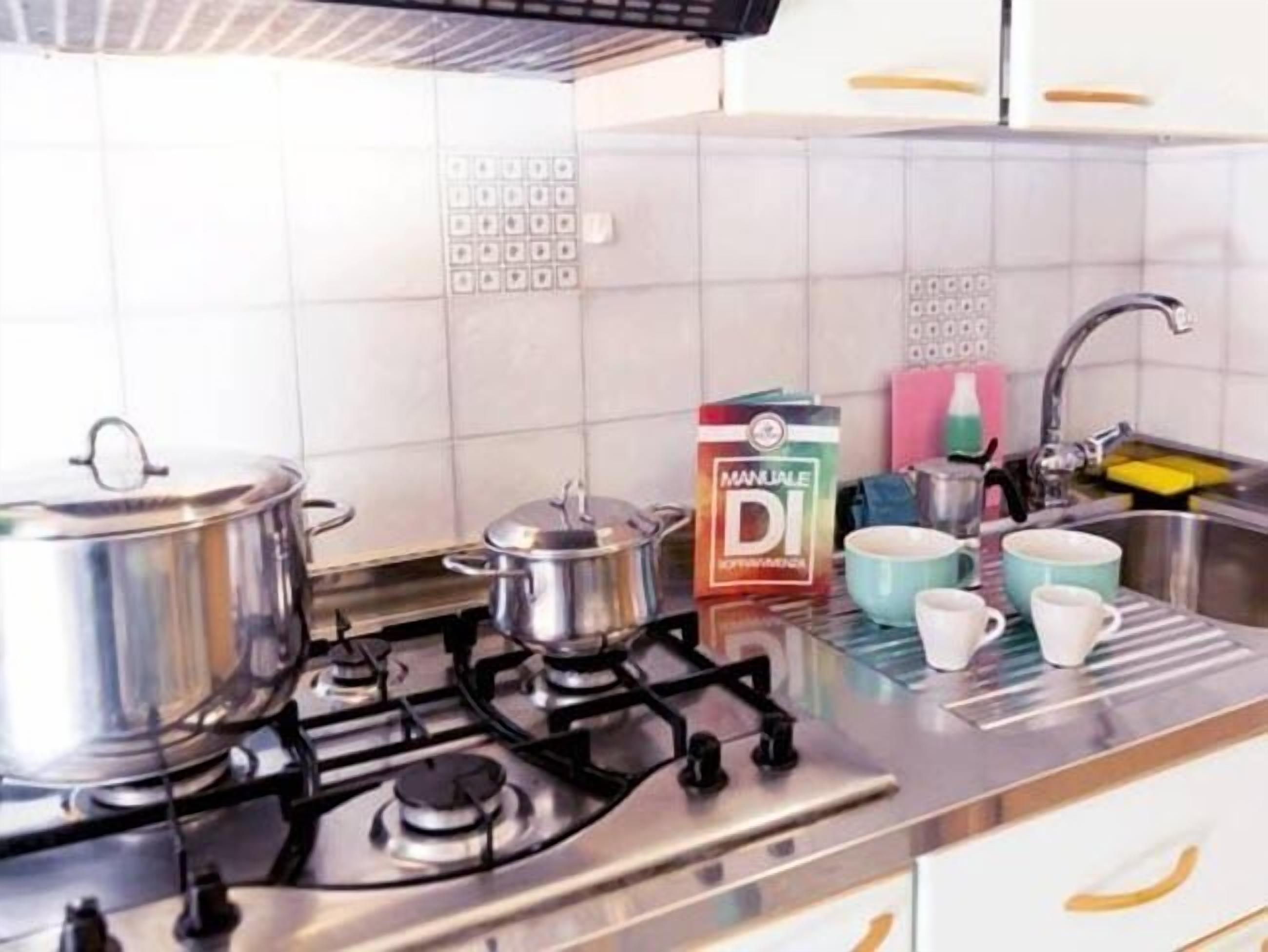 Une cuisine équipée d’une cuisinière à gaz, de casseroles, d’une boîte de « MANUAL DI » et d’un évier rempli de vaisselle.