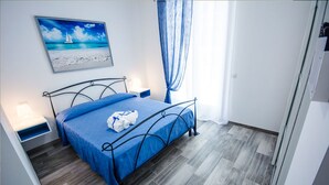 Un dormitorio ordenado con cama, mesita de noche, un cuadro en la pared y una ventana con cortinas.