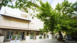 Un edificio con tejado de baldosas, un árbol grande en primer plano y un camino de entrada de grava.