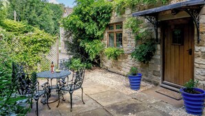 A stone building with a wooden door, a small patio with a table and chairs, and potted plants. - 2 bedroom accommodation in Uley, near Dursley (Uley, near Dursley)
