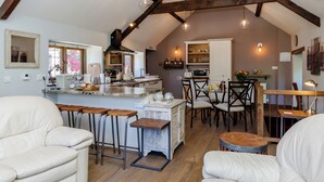 A spacious loft with exposed wooden beams, a kitchen with bar stools, and a dining area with chairs. - 2 bedroom accommodation in Uley, near Dursley (Uley, near Dursley)