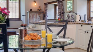 A breakfast setting with croissants, orange juice, and a glass of water on a glass table. - 2 bedroom accommodation in Uley, near Dursley (Uley, near Dursley)